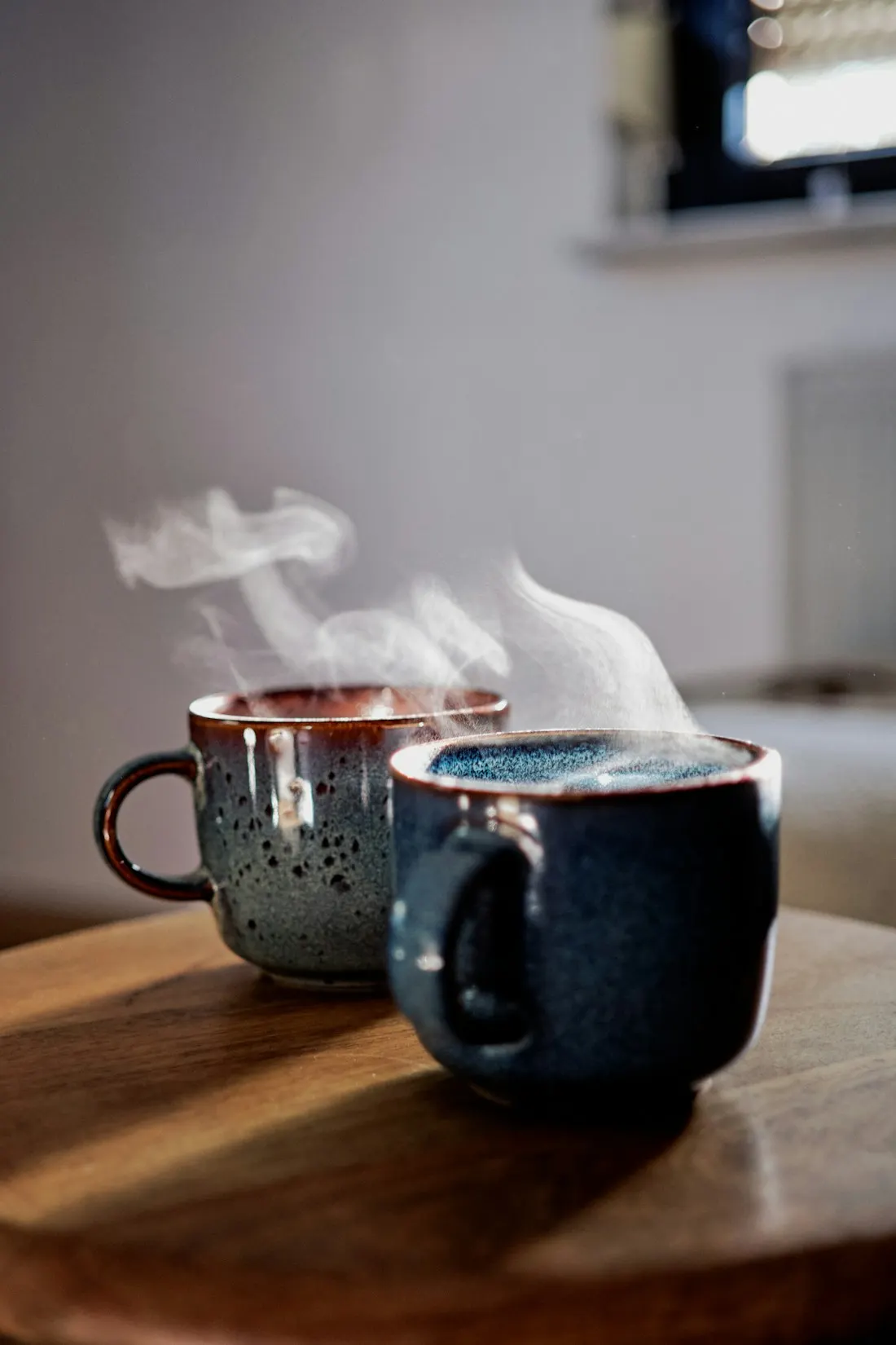 Two steaming mugs on a wooden table in morning light